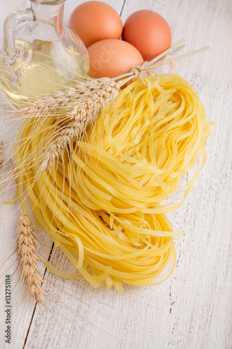 Pasta, spikelets of wheat and eggs on a white wooden background