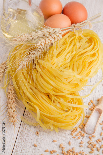 Pasta, spikelets of wheat and eggs on a white wooden background