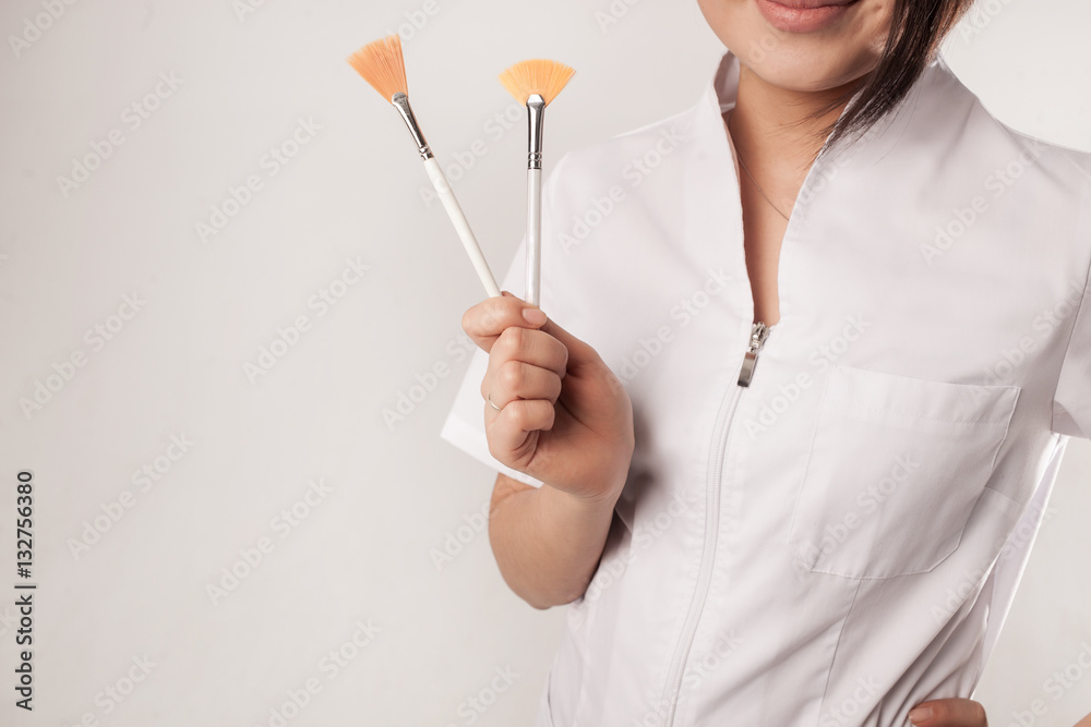 girl in medical gear holding two cosmological brushes female cosmetologist hands close up of medical stuff in hands white background studio isolated