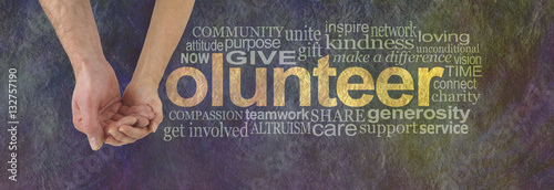 We can volunteer together - male hand cupped by a female hand making the V of VOLUNTEER surrounded by a word cloud on a rustic dark colored stone effect background photo
