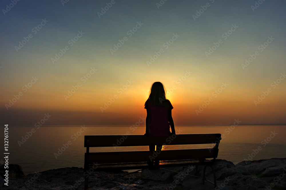 The silhouette of a lonely girl sitting on a bench on the top of the