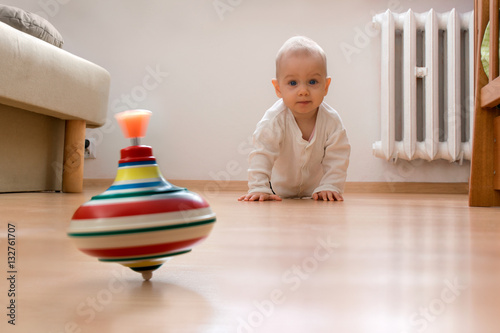 Baby on the floor is going to crawl towards spinning toy.