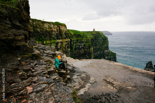 Girl sitting on cliff by ocean in Ireland