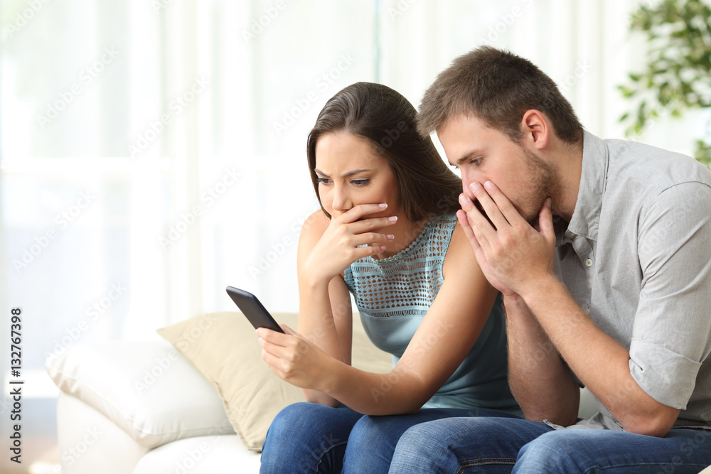 Worried couple reading bad news on the phone Worried couple reading bad news on the phone