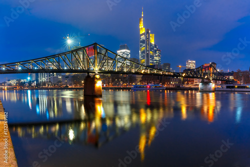 Picturesque view of Frankfurt am Main skyline and Eiserner Steg bridge with mirror reflections in the river during morning blue hour, Germany