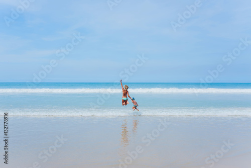 Here comes a wave. Young mother and her son jumping over the waves on the paradise beach