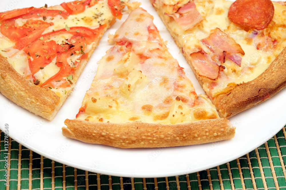 Appetizing pizza pieces on white plate on green wicker mat closeup Appetizing pizza pieces on white plate on green wicker mat closeup