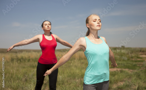 Two young women doing yoga outdoors on blue sky background posin
