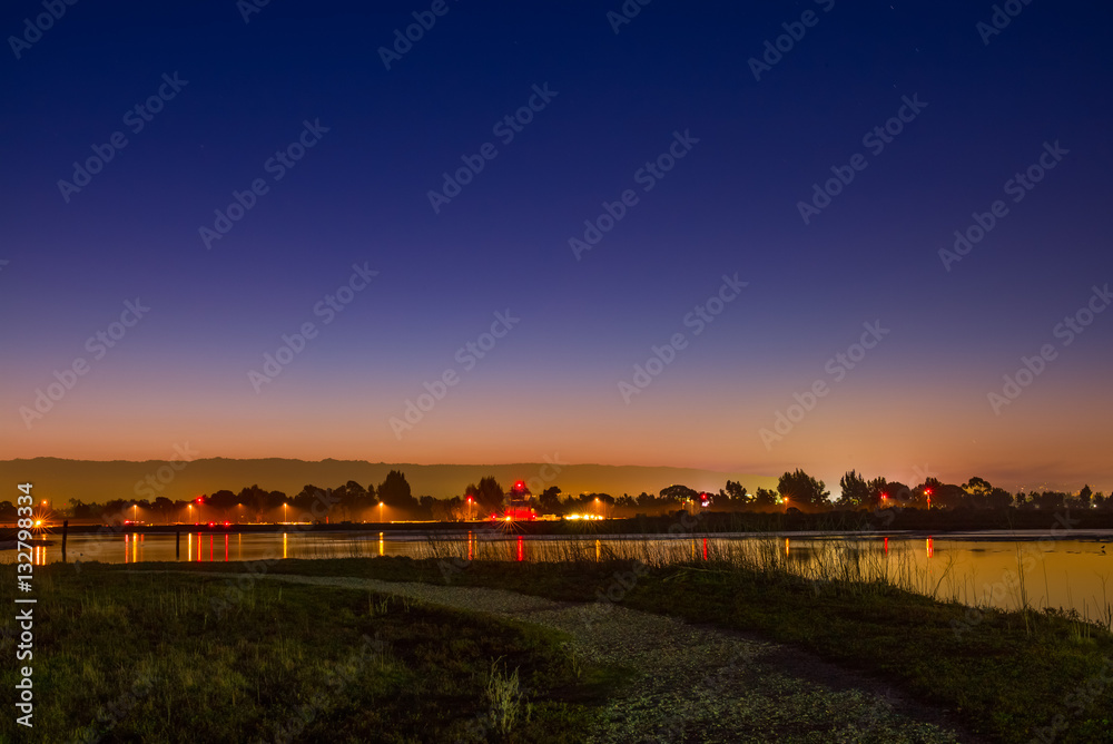Fototapeta premium A path at night overlooking the San Francisco Bay wetlands. Palo Alto airport lights at night.
