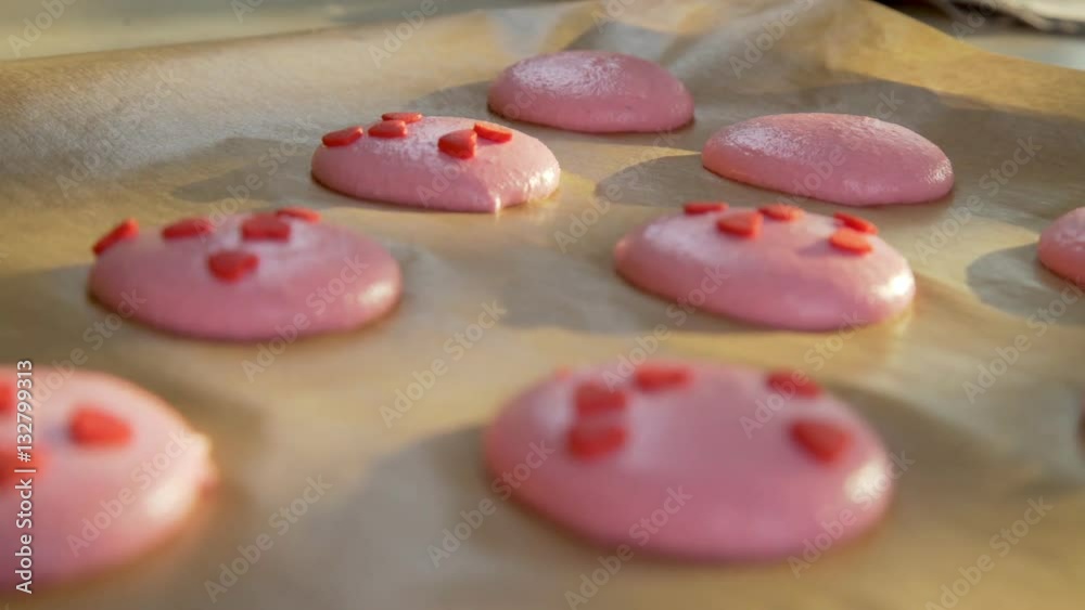 Dressing for macaroon dough elements in the shape of a heart. The shadow of the sunlight on the parchment paper. Confectioner decorate macaroon edible hearts. Treats for Valentine's Day. Dressing for macaroon dough elements in the shape of a heart. The shadow of the sunlight on the parchment paper. Confectioner decorate macaroon edible hearts. Treats for Valentine's Day.