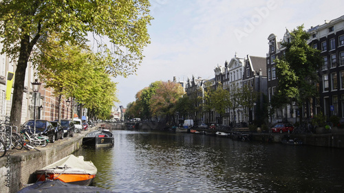 View of Amsterdam city: early morning, cloudy day, Autumn - cars and bicycles parked along the canal, trees reflected in the water - Netherlands