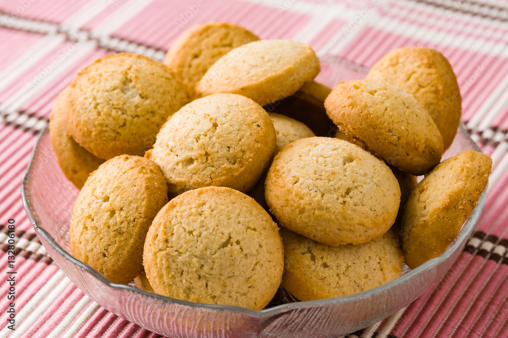 Tasty golden brown cardamom biscuits in small glass bowl on pink tablecloth.