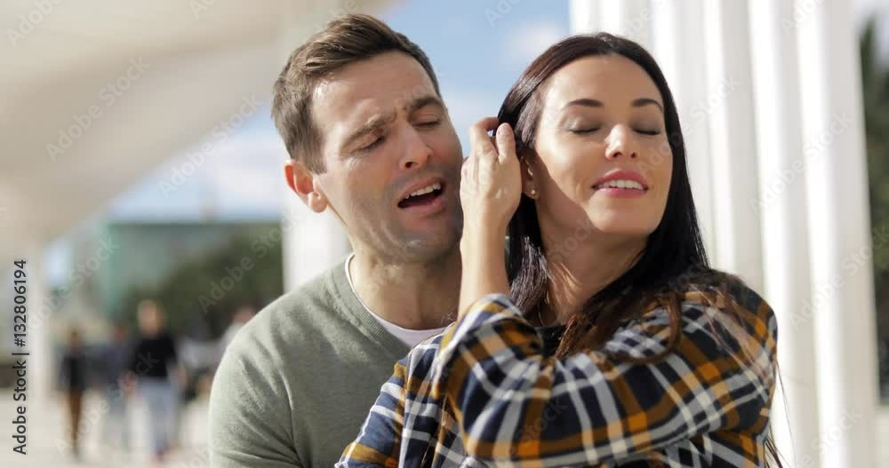 Attractive affectionate young couple relaxing at an urban waterfront sitting curled up together outdoors on a bench enjoying the sunshine Attractive affectionate young couple relaxing at an urban waterfront sitting curled up together outdoors on a bench enjoying the sunshine