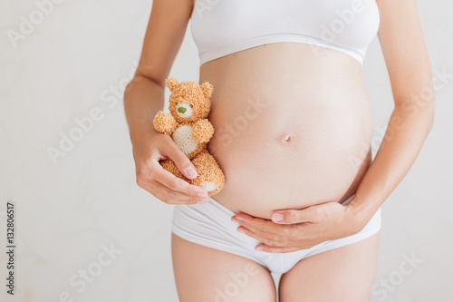 Pregnant woman in white underwear with toy bear. Young woman expecting a baby.