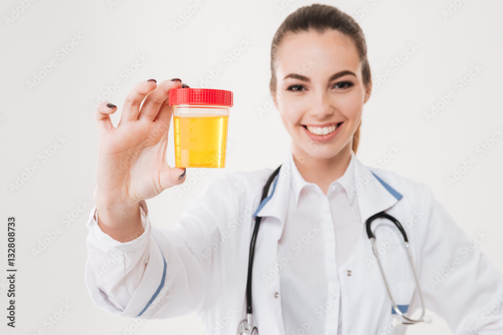 Cheerful woman doctor standing and holding bottle of urine sample Cheerful woman doctor standing and holding bottle of urine sample