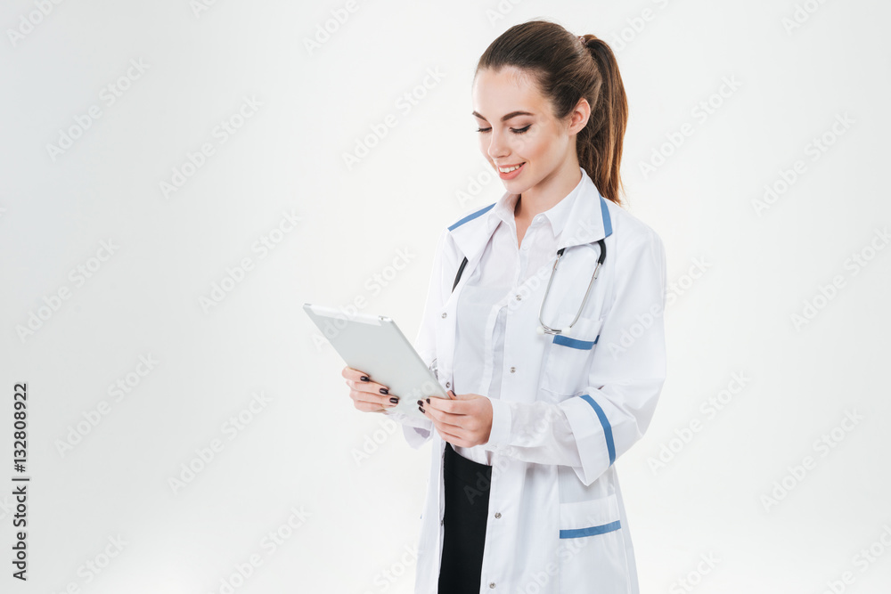 Smiling attractive young woman doctor standing and using tablet Smiling attractive young woman doctor standing and using tablet
