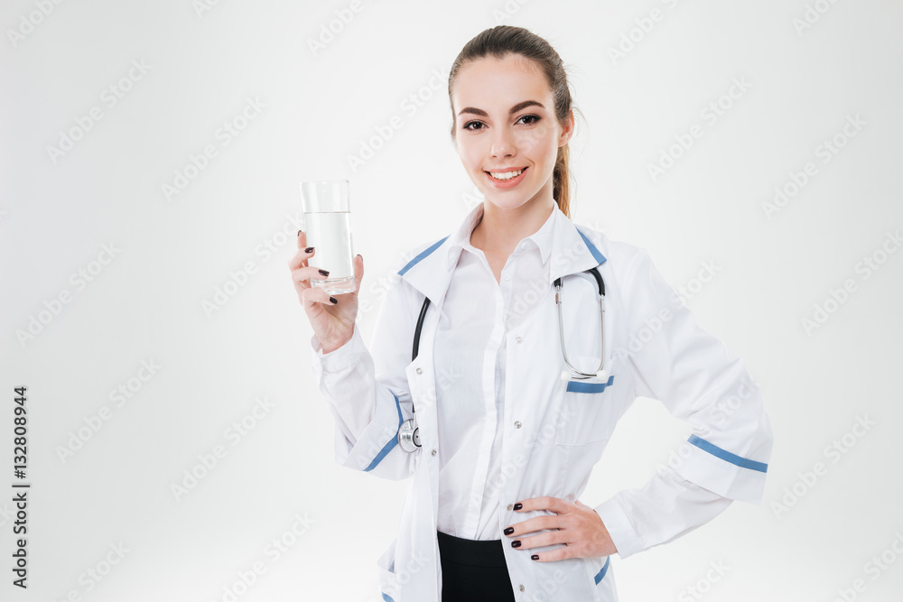 Cheerful young woman doctor standing and holding glass of water