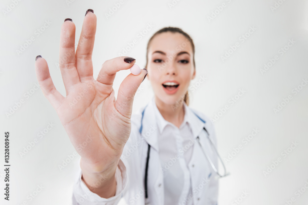 Smiling young woman doctor holding one pill Smiling young woman doctor holding one pill