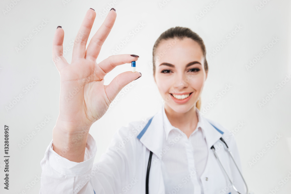 Cheerful young woman doctor standing and holding one pill Cheerful young woman doctor standing and holding one pill