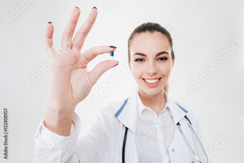 Cheerful young woman doctor standing and holding one pill