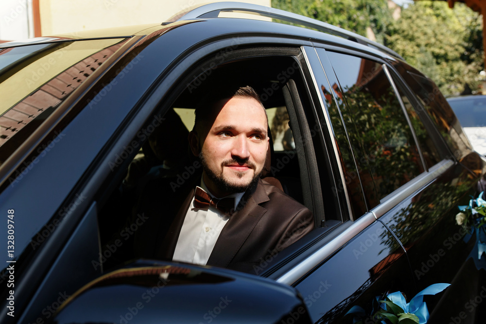 Handsome groom sits on the front seat in a black car