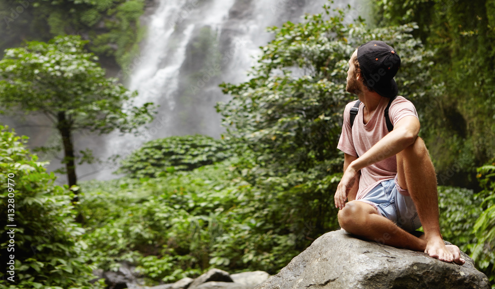 Outdoor shot of stylish young Caucasian hiker sitting barefooted Outdoor shot of stylish young Caucasian hiker sitting barefooted
