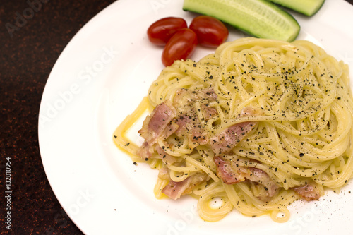 spaghetti on a white plate with fresh tomatoes and cucumbers