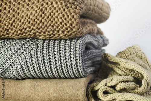 three warm sweaters and a scarf in a stack on a white wooden she