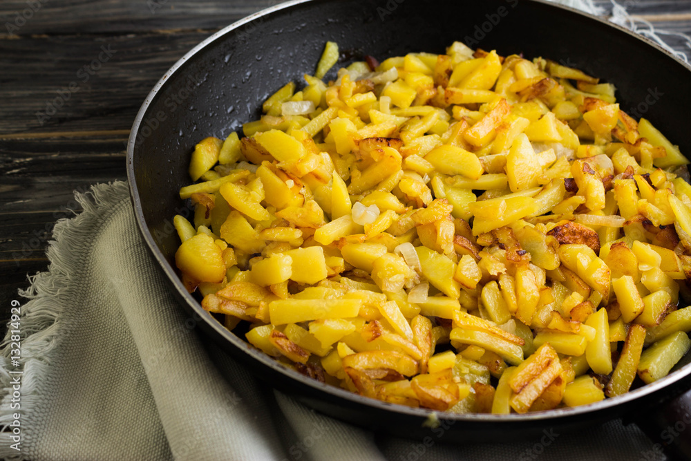 Fried potatoes in a frying pan on a wooden background in rustic style Fried potatoes in a frying pan on a wooden background in rustic style