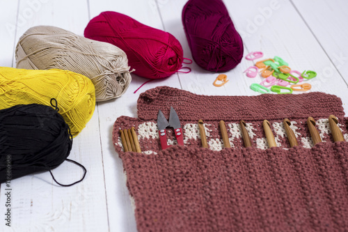 Set of bamboo crochet hooks, color sticker and colorful yarn on white wooden table.