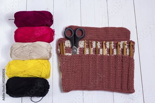 Set of bamboo crochet hooks, color sticker and colorful yarn on white wooden table.