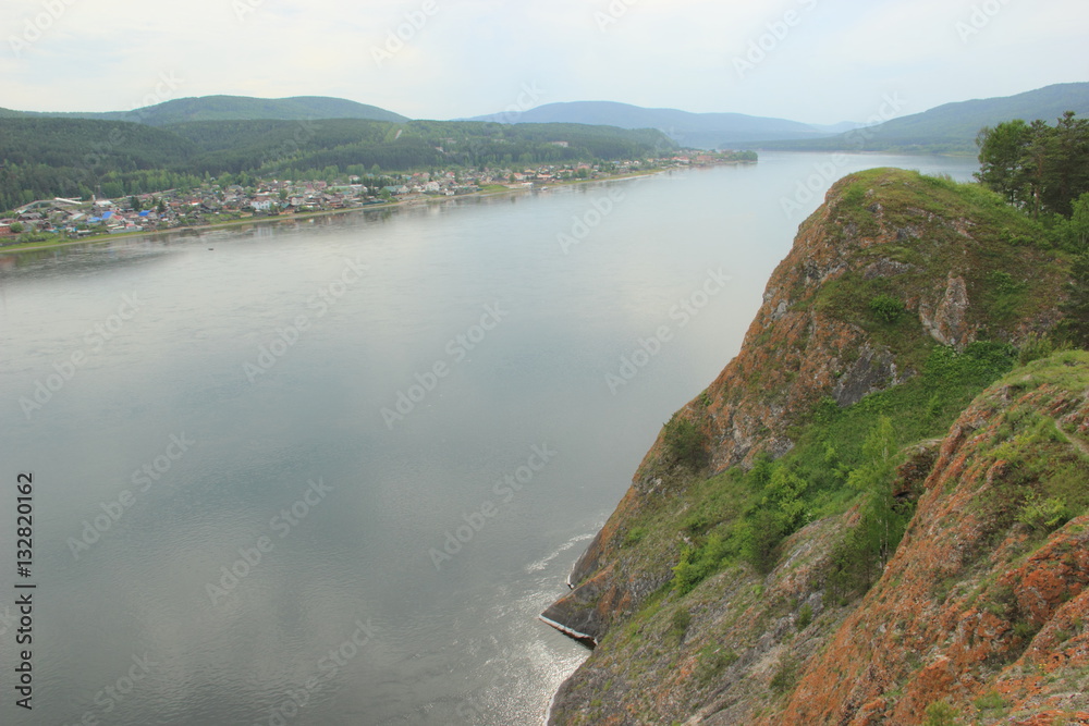 Full-flowing river Yenisei, receding into the distance in the mountains. On the left Bank is seen the village, and the right Bank is high and rocky, covered in some places with vegetation Full-flowing river Yenisei, receding into the distance in the mountains. On the left Bank is seen the village, and the right Bank is high and rocky, covered in some places with vegetation