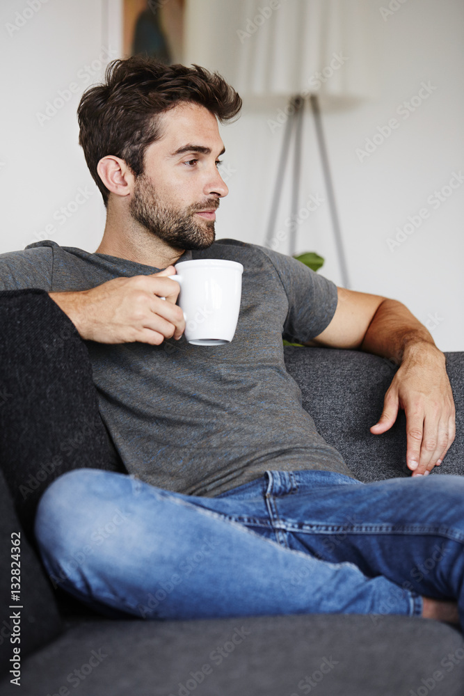 Guy enjoying coffee on couch, looking away Guy enjoying coffee on couch, looking away
