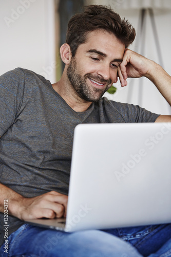 Guy at home using laptop, smiling