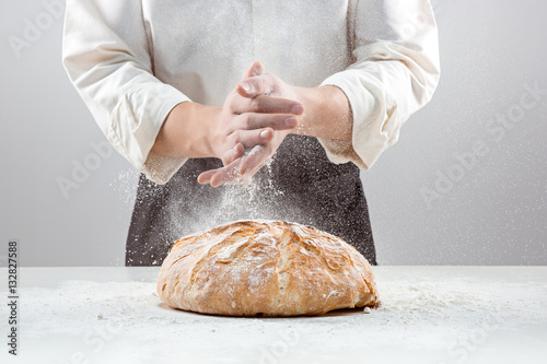 The male hands in flour and rustic organic loaf of bread photo