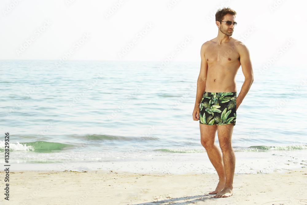 Man shirtless with shorts on beach, looking away Man shirtless with shorts on beach, looking away