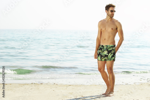 Man shirtless with shorts on beach, looking away