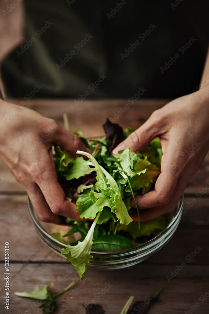 Close up of female mixing green salad in bowl. Healthy food and lifestyle concept.