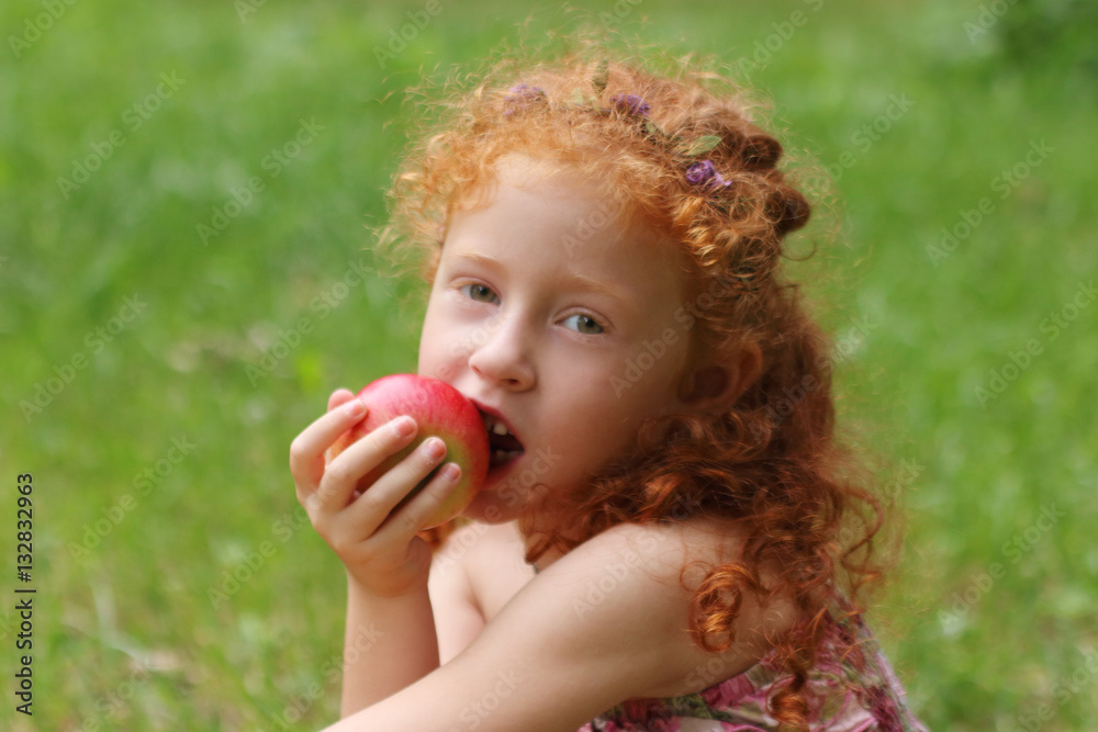 Little girl eats apple on lawn in green summer park, close up, s Little girl eats apple on lawn in green summer park, close up, s