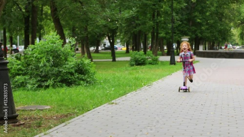 Wallpaper Mural Cute little girl with red hair rides scooter in green summer park Torontodigital.ca