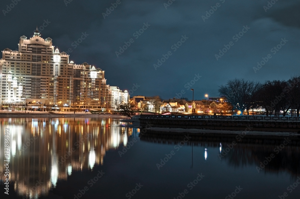Minsk city nightly landscape with reflection in Svislach river in the evening. Night scene of Trinity hill, downtown Nemiga, Nyamiha, Belarus.