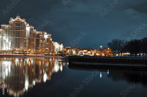 Minsk city nightly landscape with reflection in Svislach river in the evening. Night scene of Trinity hill, downtown Nemiga, Nyamiha, Belarus.