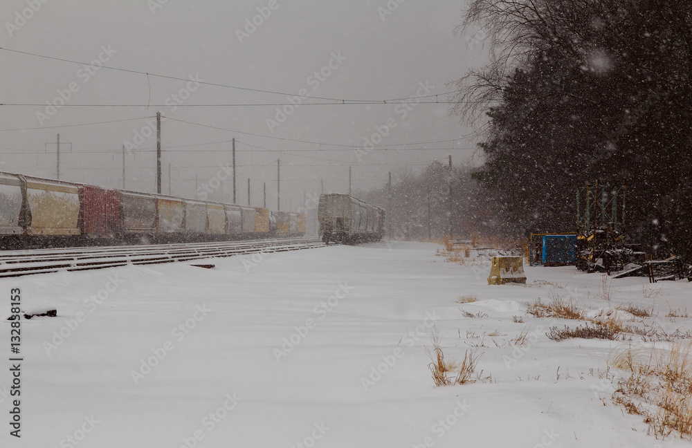 back view of Freight train running on the railway tracks in winter while is snowing