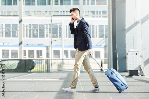business man walking with luggage on telephone call at station