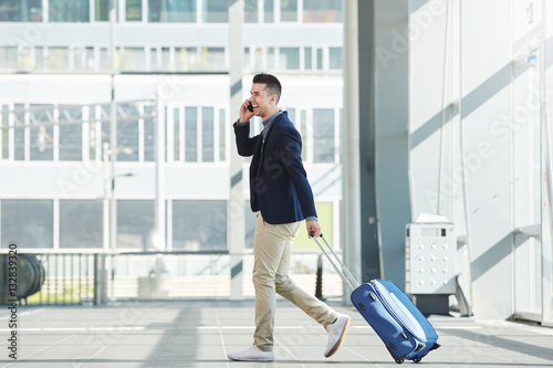 business casual man walking in station with phone and suitcase