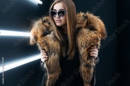 Beauty fashion glamour model girl in black coat and black trousers posing and having fun over black background with lamps,curly hairstyle,makeup,skin care body cream,long legs,retro style,foxy hair