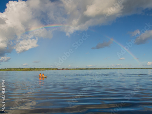 Iquitos, Peru- May 16, 2016: Rainbow over Amazon river and  kayak with the canoeists. photo