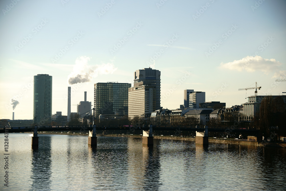 Naklejka premium Hochhäuser an der Friedensbrücke Frankfurt / Hochhäuser wie der Westhafen Tower sowie Industrie an der Friedensbrücke und entlang des Flusses Main in Frankfurt.