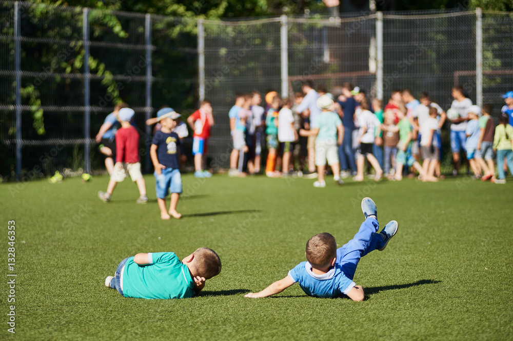 Fototapeta premium Two young little boys lie on grass at football stadium.