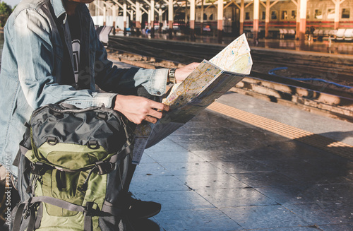 Young man backpacker waiting for train and travel bag and travel map. Travel concept.